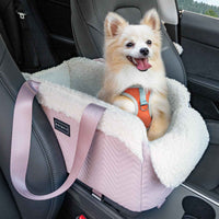 Cute small dog with fluffy fur sitting in a pink and cream plush pet car seat with safety harness, installed in a vehicle's back seat, outdoors view